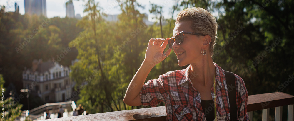 Fototapeta premium Cheerful woman in sunglasses standing in summer park, banner