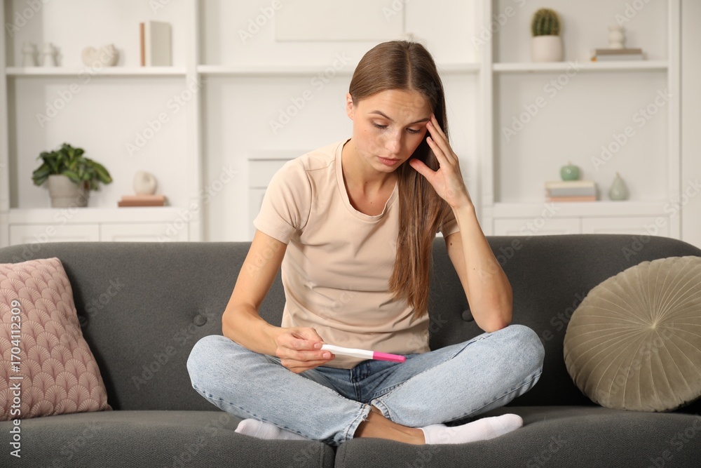 Obraz premium Worried young woman with pregnancy test on sofa at home