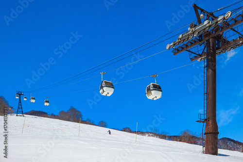 Gondola lifts going up a snowy slope under a clear blue sky (Tsugaike Kogen, Hakuba, Nagano, Japan)