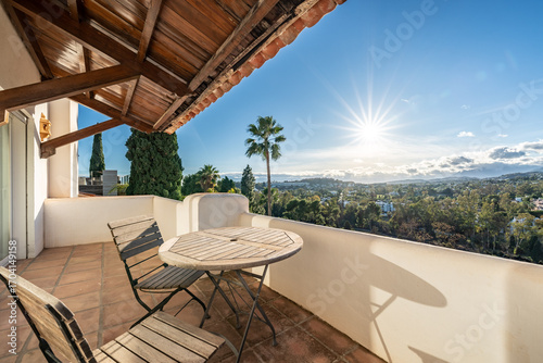Quadro su tela an image of a luxury balcony with wooden chairs and table and sunset landscape v