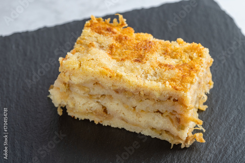 Moist layered apple semolina pie with crispy golden topping on black slate.