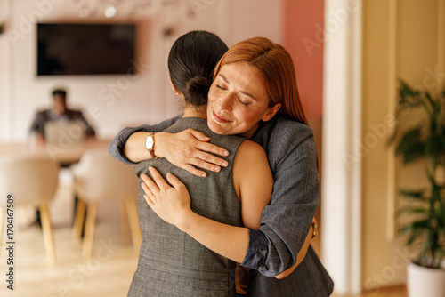 Female manager embracing coworker offering motivation and strong team connection in corporate office