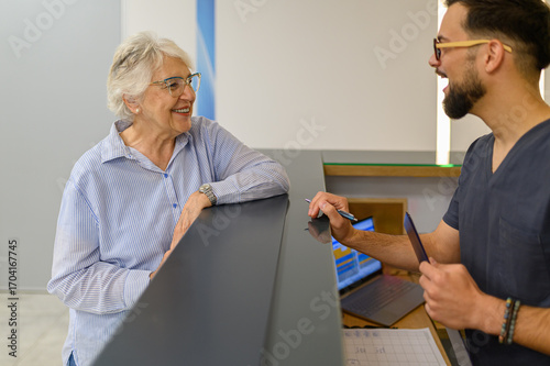 Photos Elderly woman warmly interacting with young doctor at reception counter during h