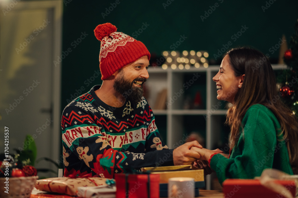 Fototapeta premium Happy couple holding hands and exchanging christmas gifts at home