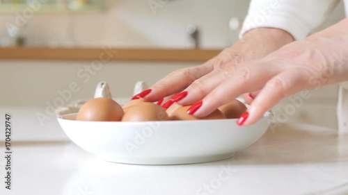 Person is preparing eggs in a white bowl. There are six eggs in the bowl. The eggs are in a row and are being cracked