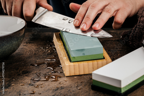 A man sharpens a knife with a grindstone on a rustic wooden table.