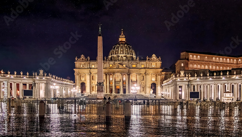 St. Peter's Basilica and the iconic obelisk in St. Peter's Square at night, with majestic illuminations reflecting on wet pavement under a starry sky in Vatican City, Rome, Italy