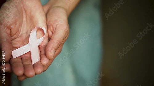 Close-up of female hands offering pink satin ribbon on open palm, symbolizing support for breast cancer patients and October awareness month.