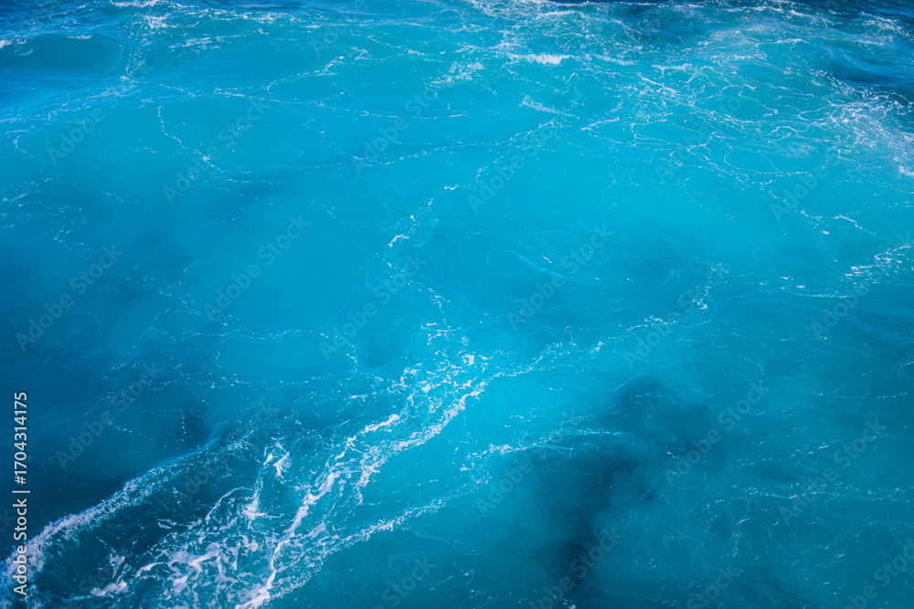 Fototapeta premium Vibrant ocean waves create a stunning blue tapestry near coastal shores during a sunny afternoon