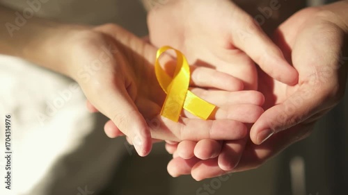 Powerful image of protective hands encircling small hands holding yellow ribbon, symbolizing unity in childhood cancer support.