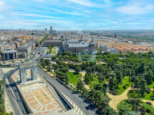 Parque del Oeste and the Arco de la Victoria stand majestically in this panoramic view of Madrid. The scene captures the vibrant mix of urban nature, monumental architecture, and everyday city life