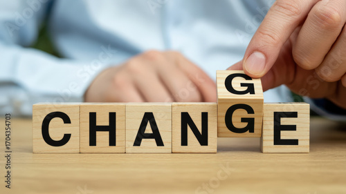 A person's hand is turning a wooden block to change the word 'CHANGE' to 'CHANGE' by flipping the letter 'G' to 'E'.