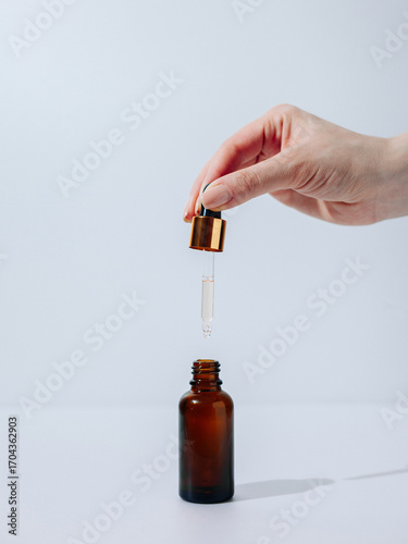 Cosmetic brown bottle, face serum, hand holding a cosmetic dropper
