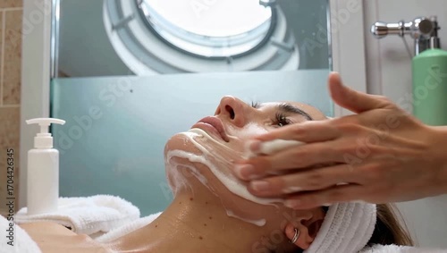 Close-up side view of a woman receiving a facial massage with cleansing foam in a spa treatment room, skin care and beauty concept