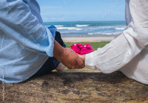 couple looking at the sea sitting on a tree trunk with baby shoes, first-time mother and father