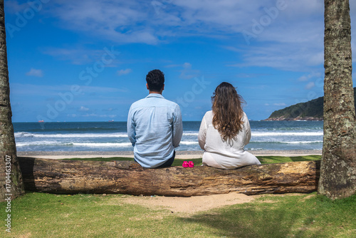 couple looking at the sea sitting on a tree trunk with baby shoes, first-time mother and father