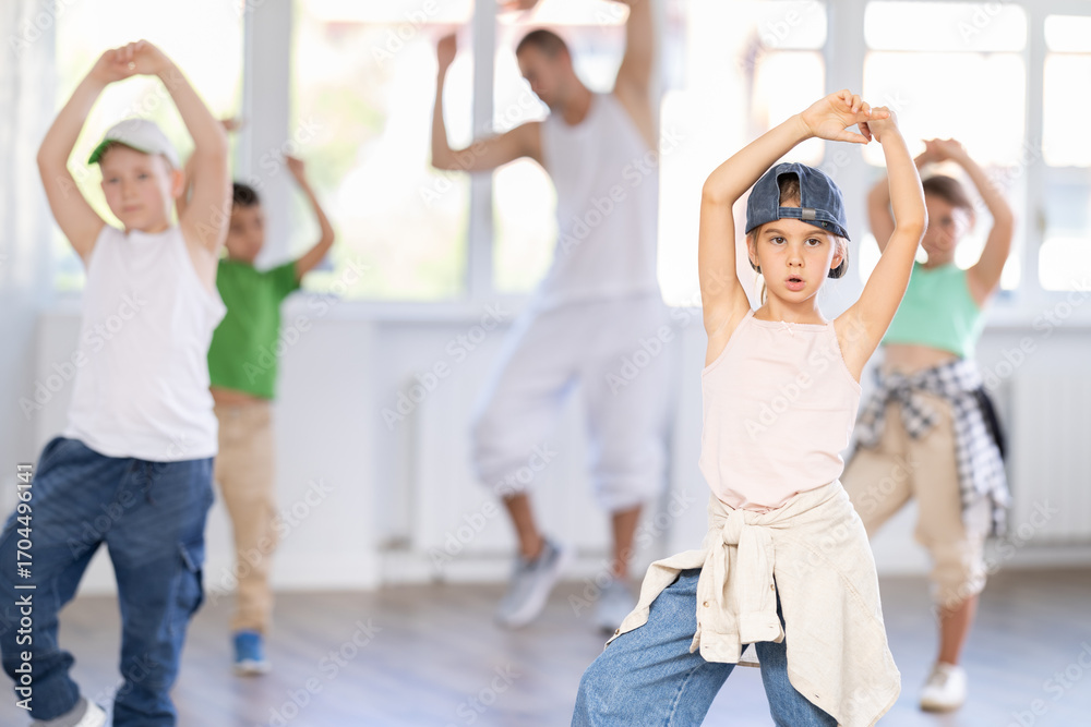 Naklejka premium Focused preteen girl performing dynamic hip hop moves in group class for kids, led by skilled young male dance instructor in vibrant urban studio