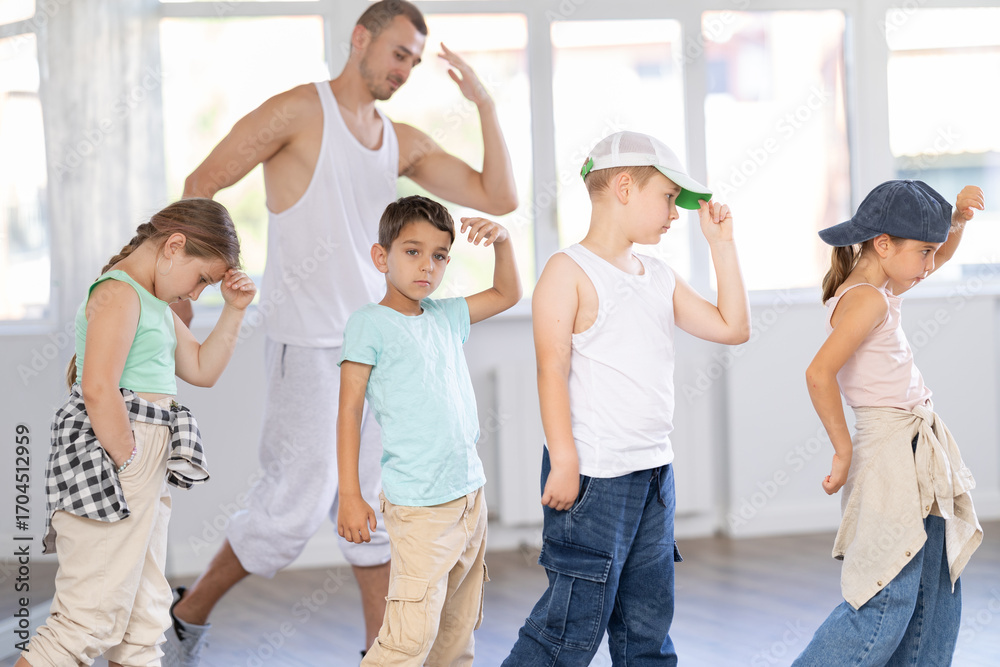 Fototapeta premium In sports studio, creative childrens team learns hip-hop dance accompanied by experienced man teacher