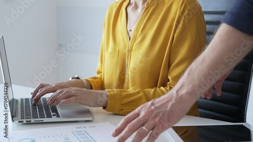 Colleagues or partners are collaborating on a project, analyzing financial charts and using a laptop to input data, working together to achieve their business goals. Business people