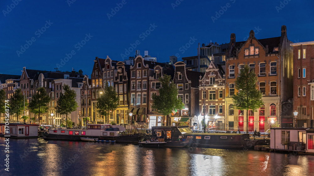Obraz premium Panoramic timelapse hyperlapse of the illuminated famous Dancing Houses along the Amstel River day to night transition. Amsterdam, Netherlands