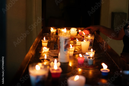 Photograph of a woman placing candles on an altar inside a religious center or church in a dark place with bright candles