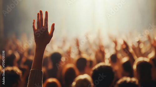 Raised hand in a crowd with warm, soft lighting capturing a moment of participation, unity, and anticipation among many blurred people