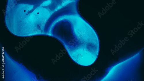 Fluid texture. Liquid mix. Defocused blue neon color water drop glow paint ink dark black flow oil blob floating on abstract light background.