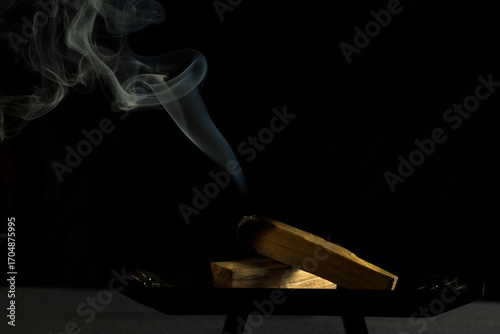 Palo Santo wood burning with smoke on black background