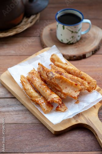 Several pieces of piscok, or banana chocolate, with a crispy golden-brown skin are arranged on white parchment paper on a wooden cutting board