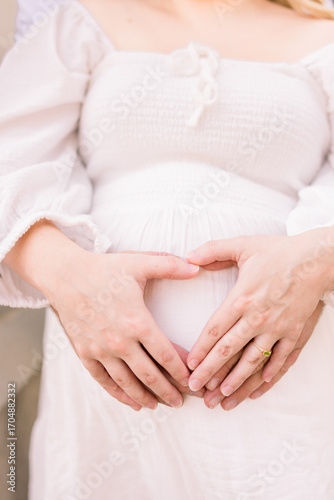 A pregnant woman has her hands in a heart on top of her husband's hands