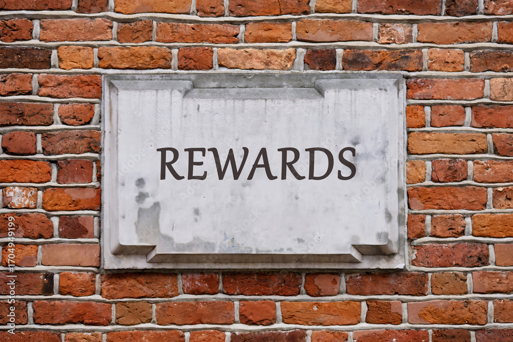 Fototapeta premium Business and Risk or Reward concept. Copy space. REWARDS written on a plaque on a weathered brick wall.