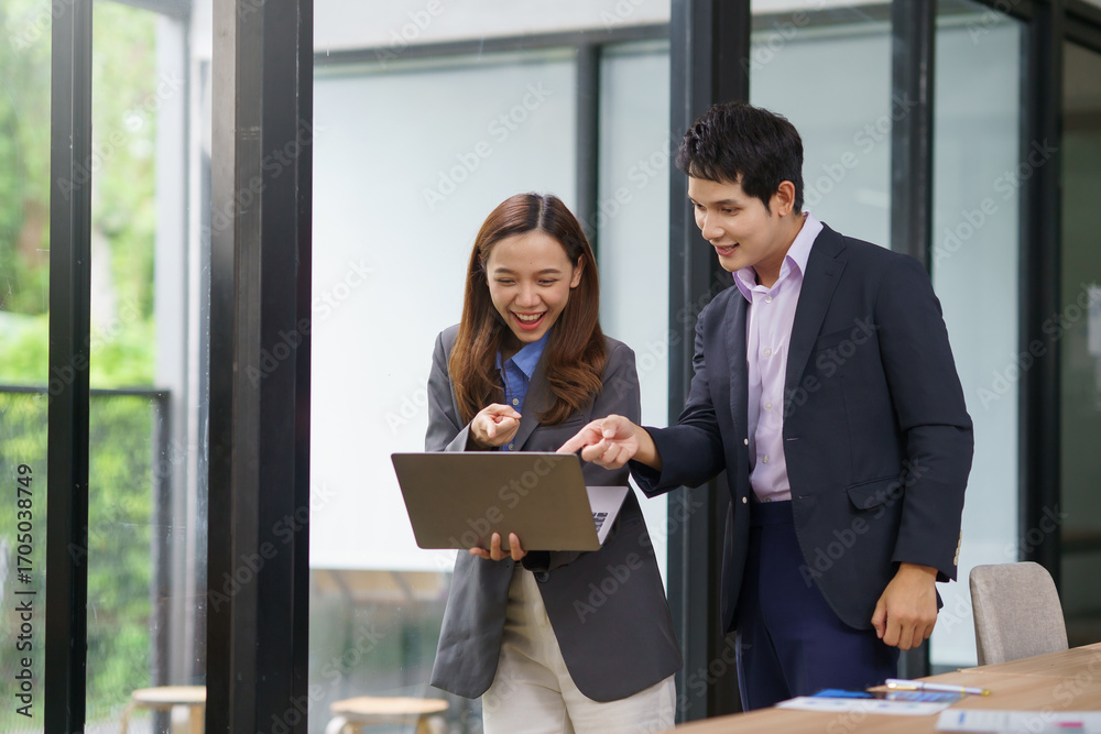 Businesswoman holding a laptop and engaging in a discussion with a businessman inside a modern office, fostering collaboration and teamwork Businesswoman holding a laptop and engaging in a discussion with a businessman inside a modern office, fostering collaboration and teamwork