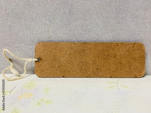 A image shows a bookmark made of cork. It's a rectangular shape with rounded corners and has a small hole on the left side where a piece of white string is threaded through. The bookmar