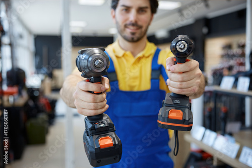 A man worker is holding impact and power drills in his hands in a store