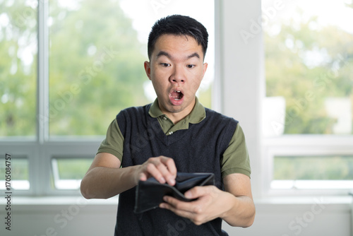 Teenage male looking surprised while checking an empty wallet, conveying financial anxiety or money problems at home.