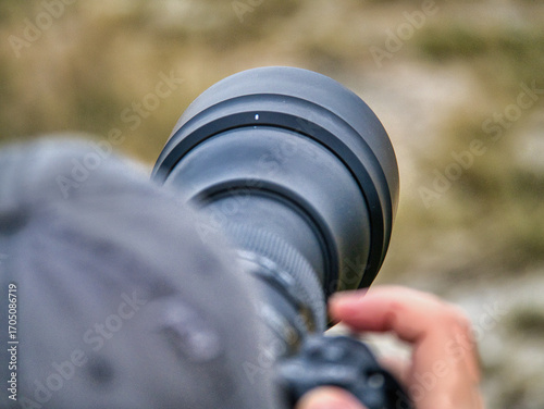 Close-up of a photographer using a large telephoto lens, focusing on wildlife or nature photography. Professional outdoor photography concept, perfect for themes of camera gear, adventure, and travel.