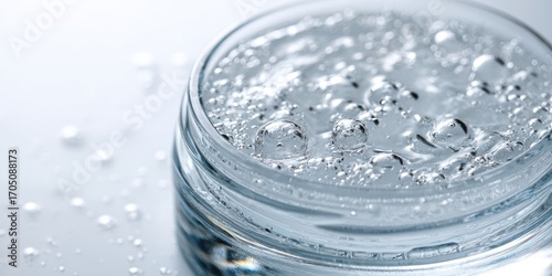 Close-up of a clear, glass jar filled with a light, bubbly gel-like substance; water droplets are scattered nearby
