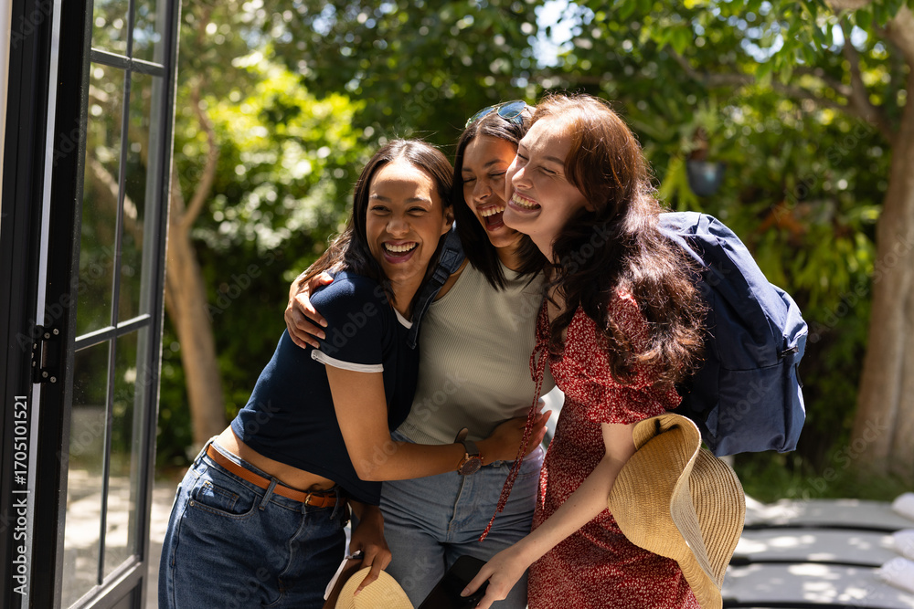 Fototapeta premium Laughing and embracing, three young women enjoy sunny day outdoors