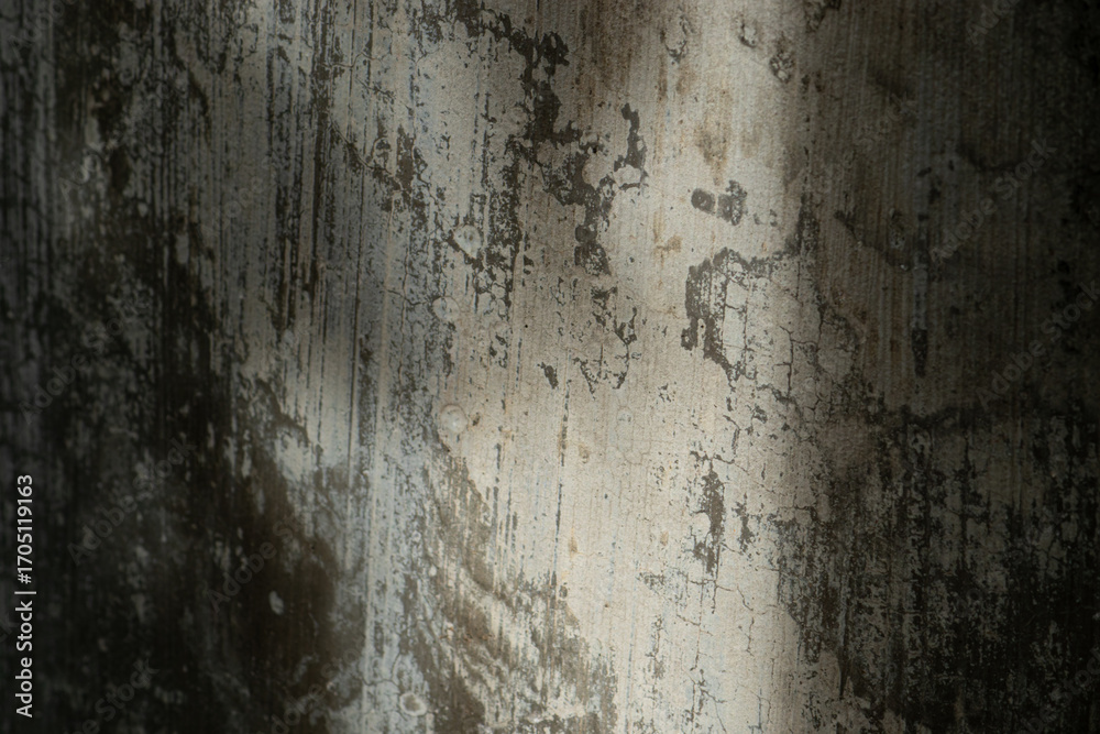 Fototapeta premium An abstract texture background of an old, peeling concrete wall with a diagonal sunbeam.