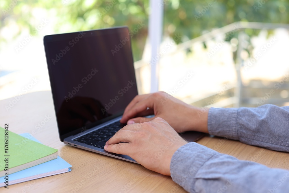 Fototapeta premium Man working on laptop at wooden table indoors, closeup