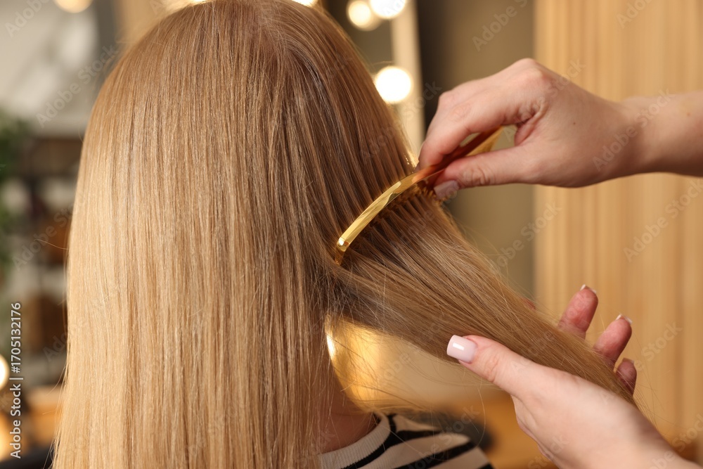 Fototapeta premium Hairstylist combing woman's hair in salon, closeup