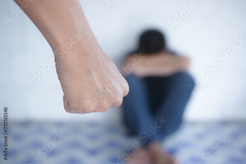A frightened, crying child is sitting in the corner of the room. Violence against children in the family. The male father holds the belt in his hand.