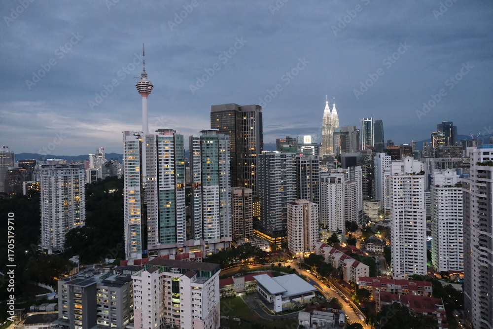 Fototapeta premium Panoramic view of Kuala Lumpur skyline at dusk featuring Kuala Lumpur Tower and Petronas Twin Towers among tall modern buildings.