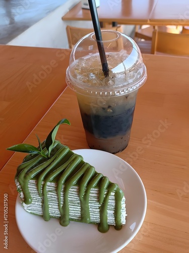 Aesthetic Cake and Refreshing Beverage: A delectable slice of green tea cake sits invitingly next to a refreshing iced drink on a wooden table, capturing the essence of a pleasant cafe experience.