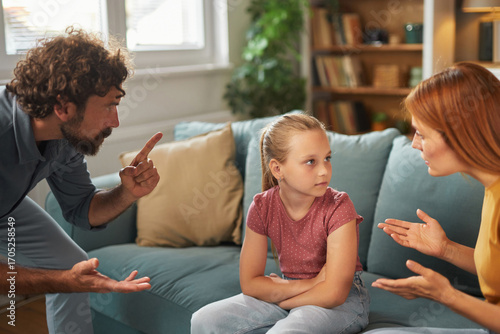 Fotografie Parents engage in a serious discussion in the living room while their daughter looks worried and upset, seated on the couch with crossed arms and listening intently to them