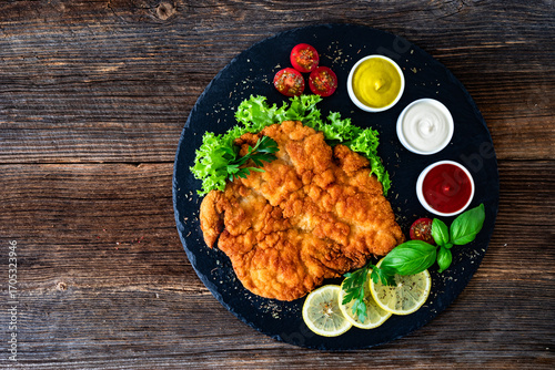 Garnished wiener schnitzel with ketchup, mayonnaise and mustard on wooden table
