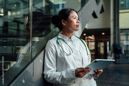 Doctor in lab coat with stethoscope using tablet at modern clinic