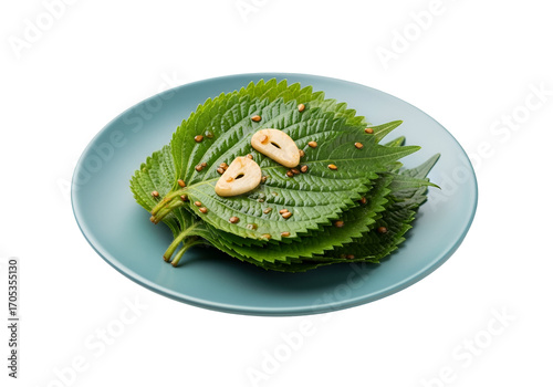 Stacked perilla leaves with garlic slices and sesame seeds on a light teal plate against a black backdrop.