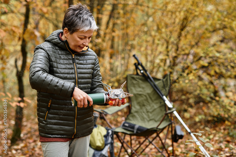Naklejka premium Senior woman enjoys a peaceful moment cooking in the forest while hiking