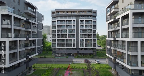 Drone shot of modern residential buildings in Kraków, Poland, featuring balconies, contemporary design, and a central playground surrounded by landscaped green areas.